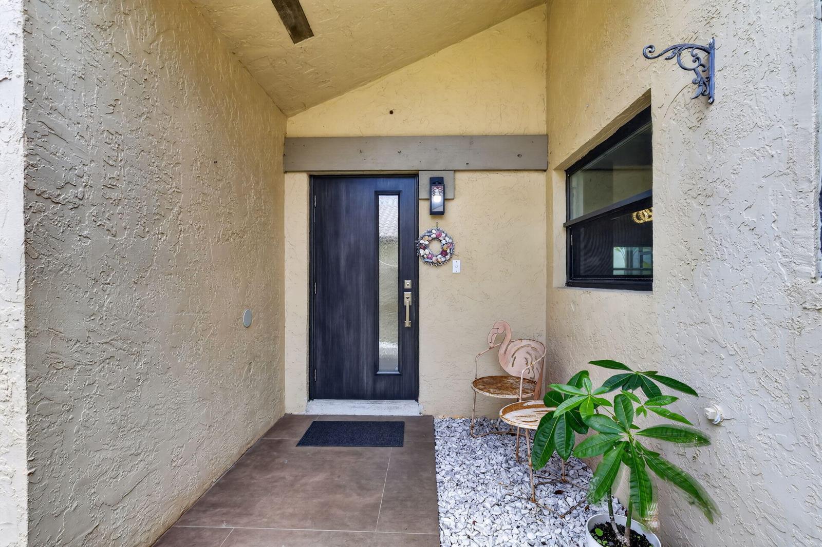 An exterior entryway features a dark wood door, stucco walls, tile flooring, and a small plant — 1230 NW 22nd Avenue, Delray Beach FL 33445, DELRAY BEACH, FL