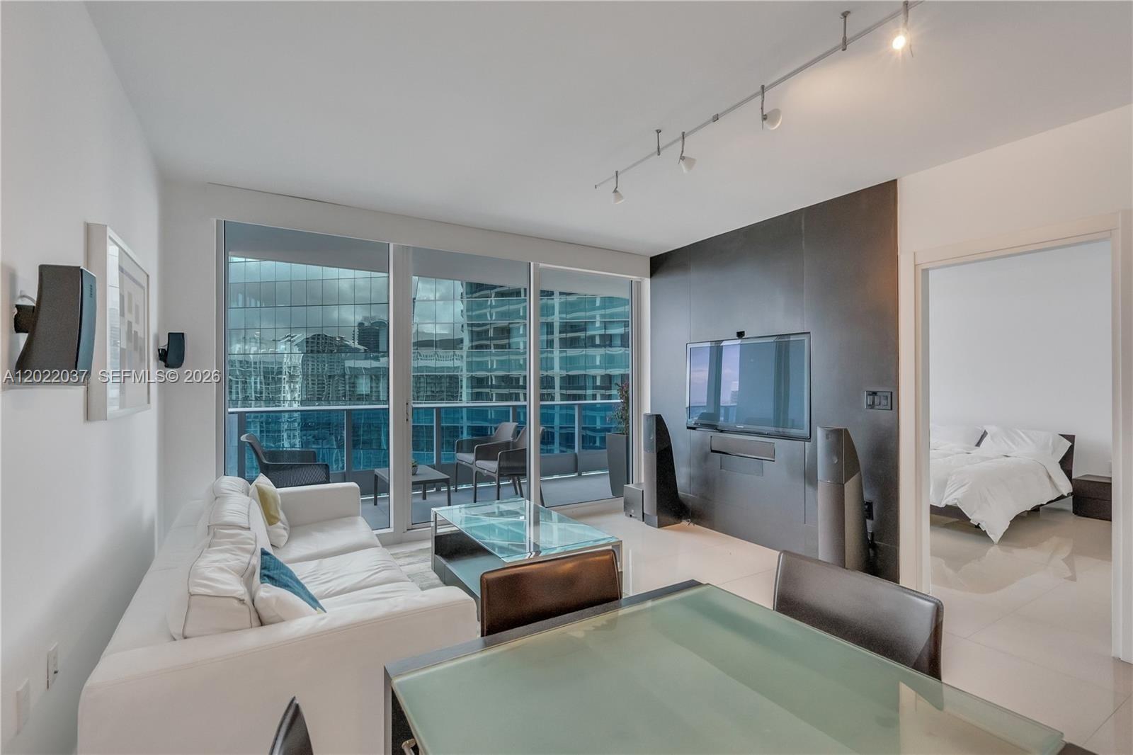 A modern living room features a white sofa, glass coffee table, and a balcony view — 200 Biscayne Boulevard Way # 3911, Miami FL 33131, MIAMI, FL