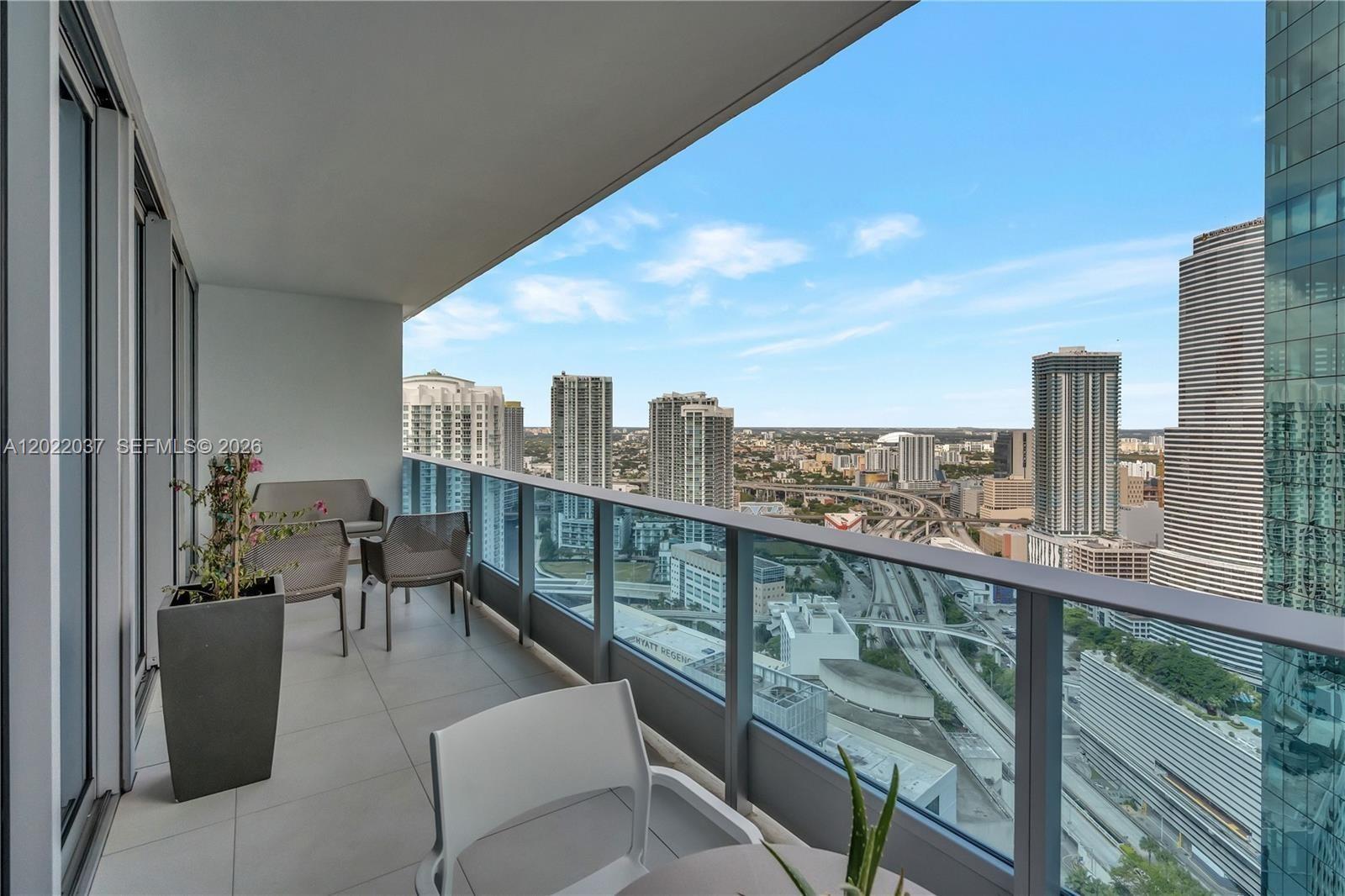 A high-rise balcony features outdoor furniture, a potted plant, and a panoramic city skyline view — 200 Biscayne Boulevard Way # 3911, Miami FL 33131, MIAMI, FL