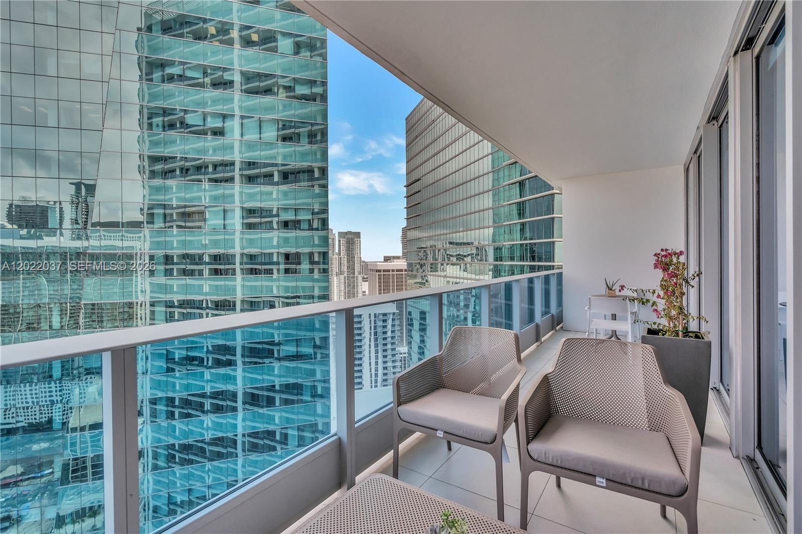 A balcony with two chairs and a small table overlooks a dense urban skyline — 200 Biscayne Boulevard Way # 3911, Miami FL 33131, MIAMI, FL