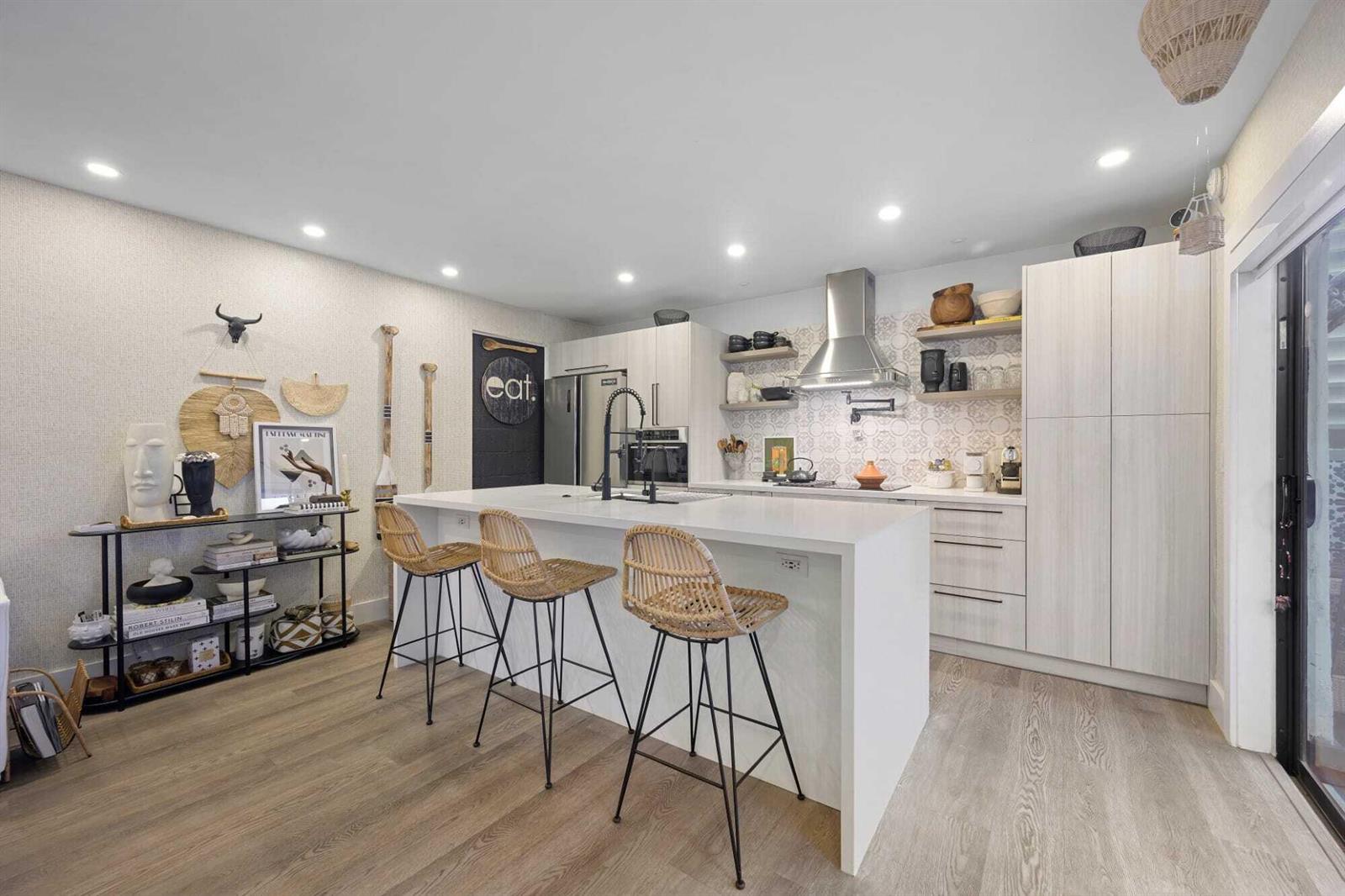 A modern kitchen features a white island with rattan stools, light wood cabinetry, and patterned backsplash — 1605 S Us Highway 1 # 10c, Jupiter FL 33477, JUPITER, FL