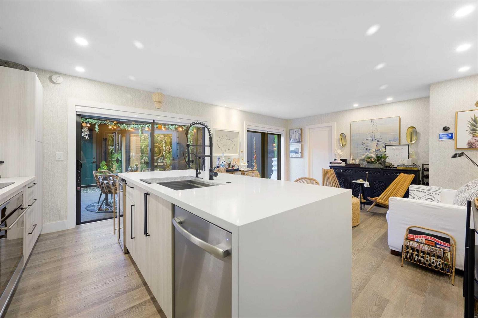 A modern kitchen features a white island with a sink, light wood cabinetry, and sliding doors — 1605 S Us Highway 1 # 10c, Jupiter FL 33477, JUPITER, FL