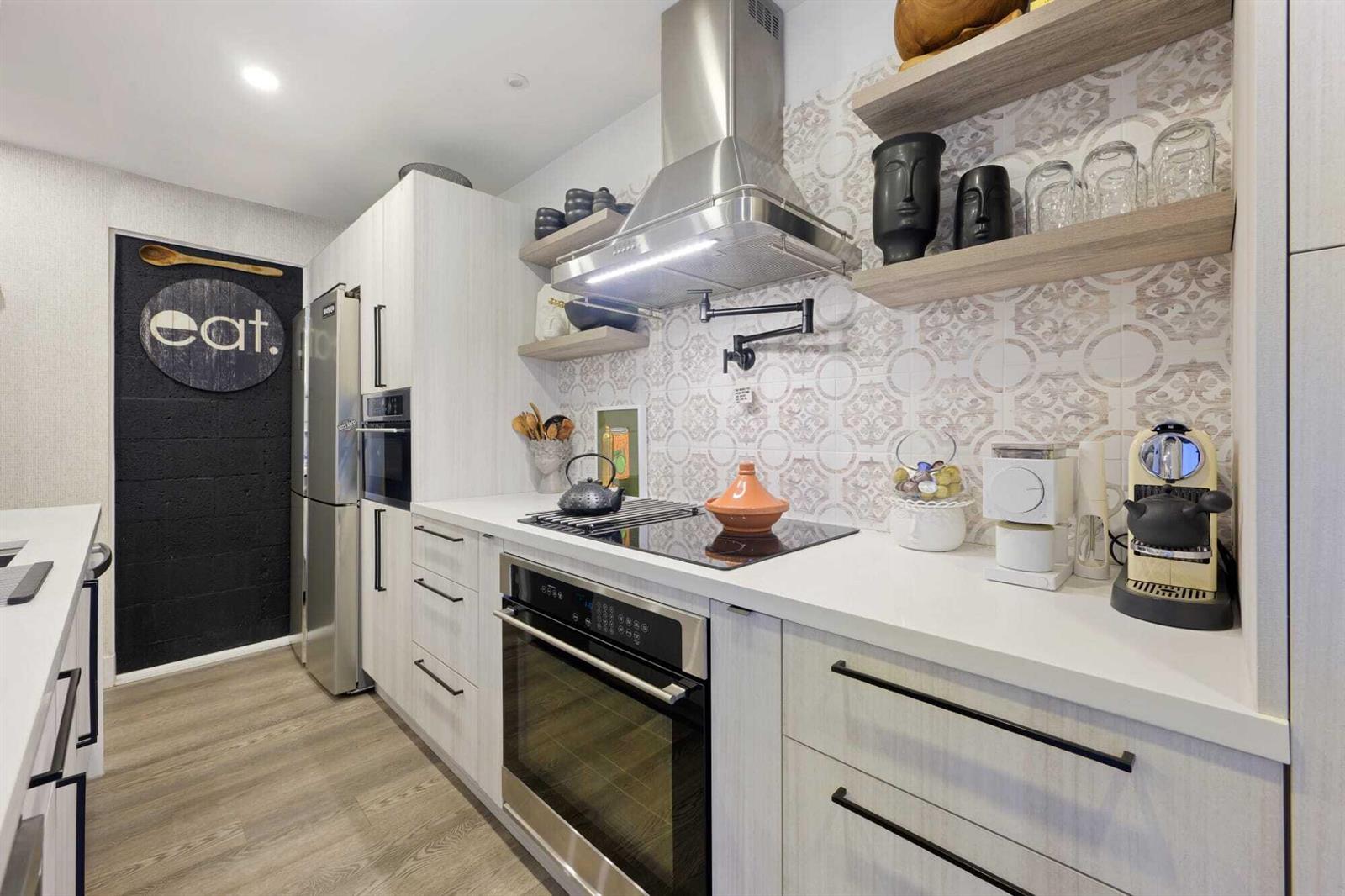 A modern kitchen features light wood cabinetry, white countertops, patterned tile backsplash, and stainless appliances — 1605 S Us Highway 1 # 10c, Jupiter FL 33477, JUPITER, FL