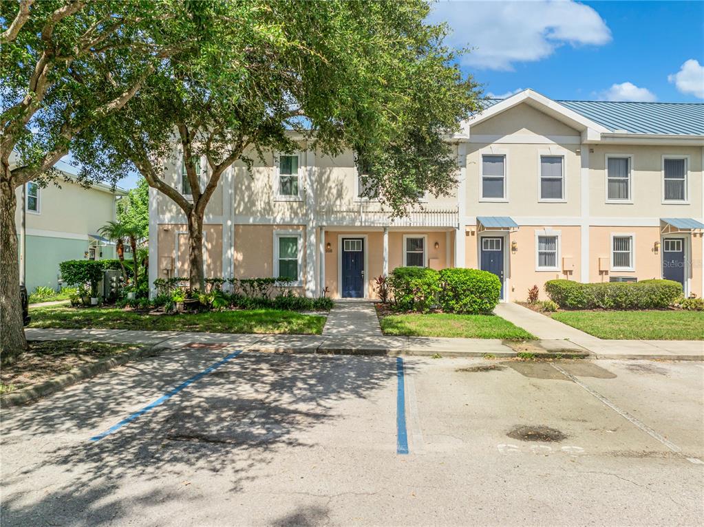A two-story townhouse exterior with a parking lot in the foreground and mature trees — 608 CORNERSTONE DRIVE, KISSIMMEE, FL