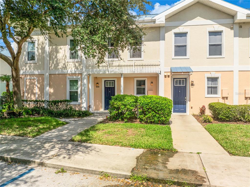 A two-story townhouse exterior with beige stucco walls, blue doors, and a front lawn — 608 CORNERSTONE DRIVE, KISSIMMEE, FL