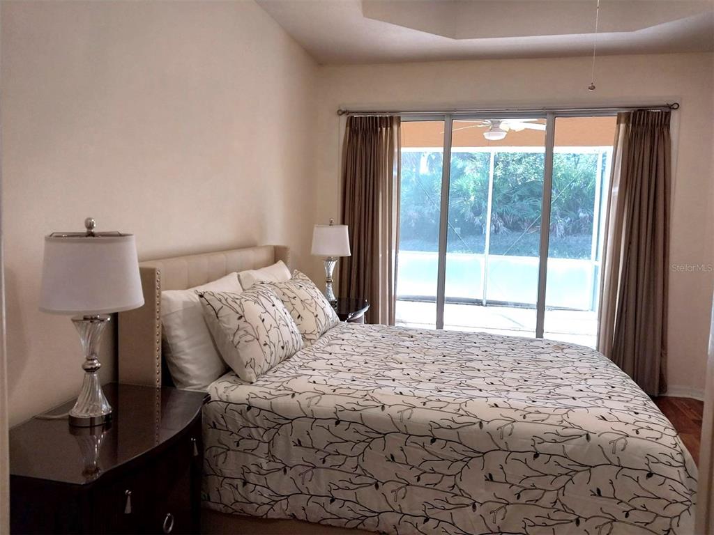 A bedroom with a bed, two lamps, and sliding glass doors leading to a screened patio — 5641 HIDDEN OAK COURT, NORTH PORT, FL