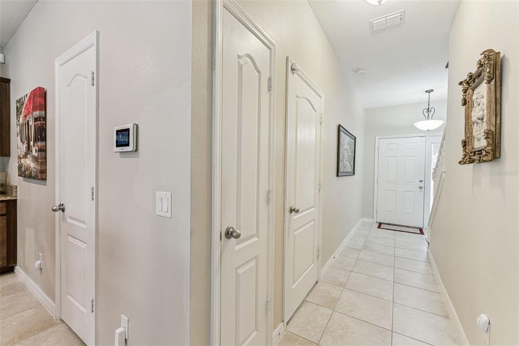A tiled hallway features multiple white doors, a thermostat, and wall-mounted artwork — 1224 PETERSON PLACE, SANFORD, FL