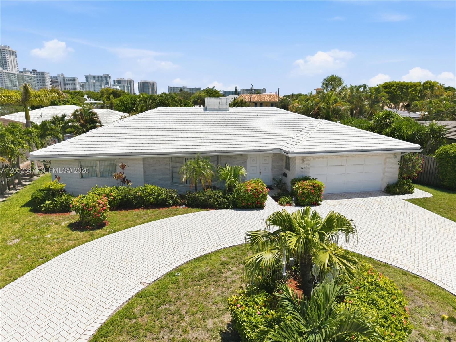A single-story house with a white tiled roof, brick driveway, and landscaping under a blue sky — 8 Castle Harbor Is, Fort Lauderdale FL 33308, FORT LAUDERDALE, FL