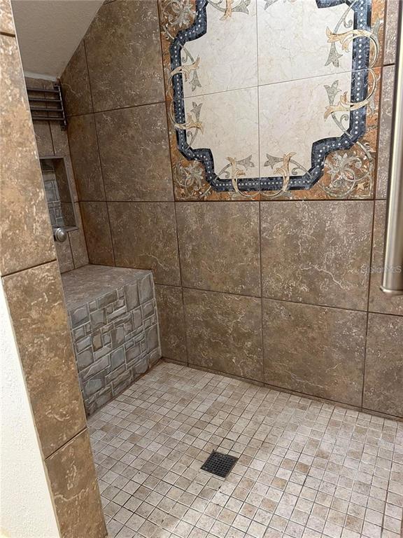 A tiled walk-in shower features a built-in bench, a decorative tile inlay, and a drain — 2212 SAN VITTORINO CIRCLE UNIT 28-107, KISSIMMEE, FL