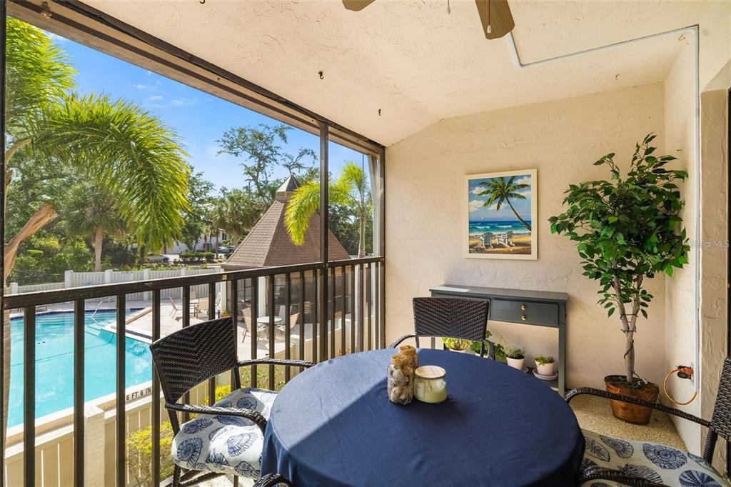 A screened-in balcony features a round table, chairs, a potted plant, and a pool view — 7201 CURTISS AVENUE UNIT 2D, SARASOTA, FL