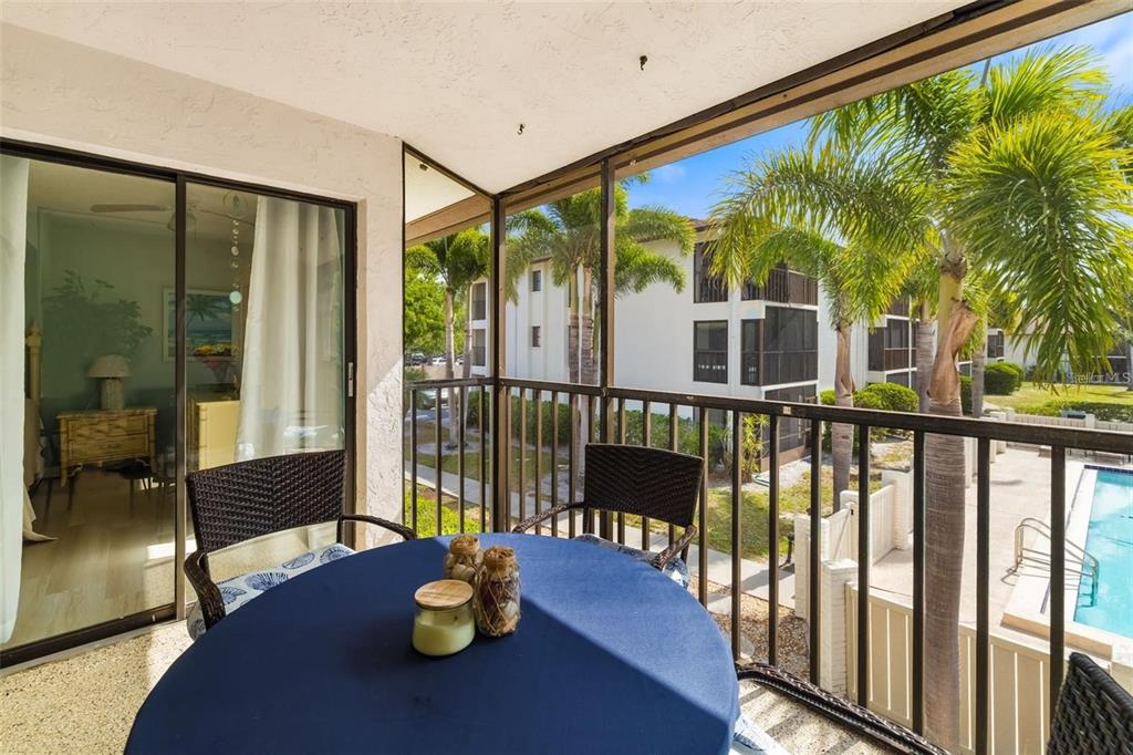 A screened-in balcony features a round table with chairs overlooking a swimming pool and palms — 7201 CURTISS AVENUE UNIT 2D, SARASOTA, FL