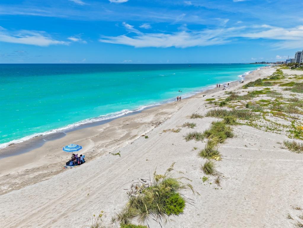An aerial view of a sandy beach with turquoise water and a blue beach umbrella — 624 FLAMINGO DRIVE UNIT 112, VENICE, FL