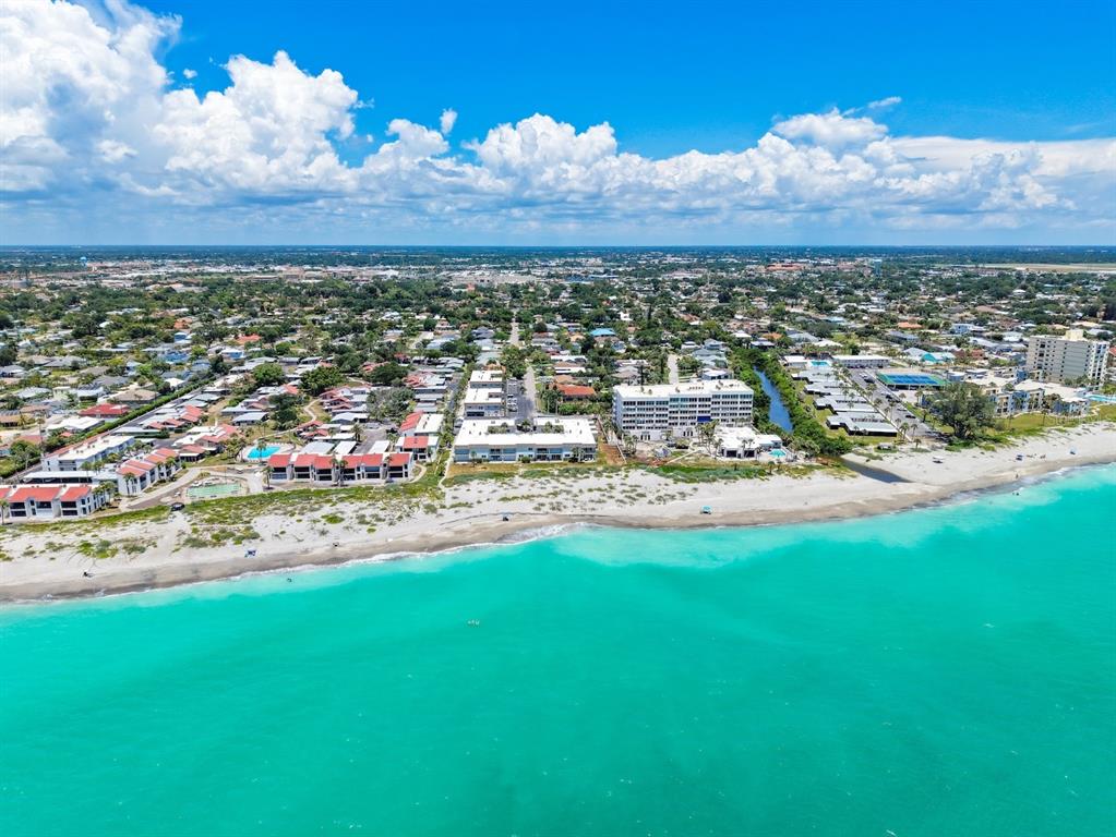 An aerial view shows a beach with turquoise water, residential buildings, and a coastal town — 624 FLAMINGO DRIVE UNIT 112, VENICE, FL