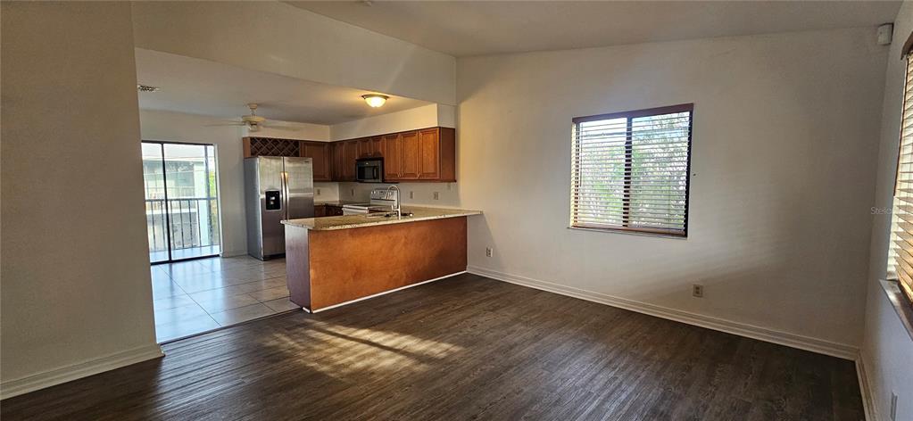 An open-concept living area features wood-look flooring, a kitchen with wood cabinets, and a balcony — 4904 VINCENNES COURT UNIT 209, CAPE CORAL, FL