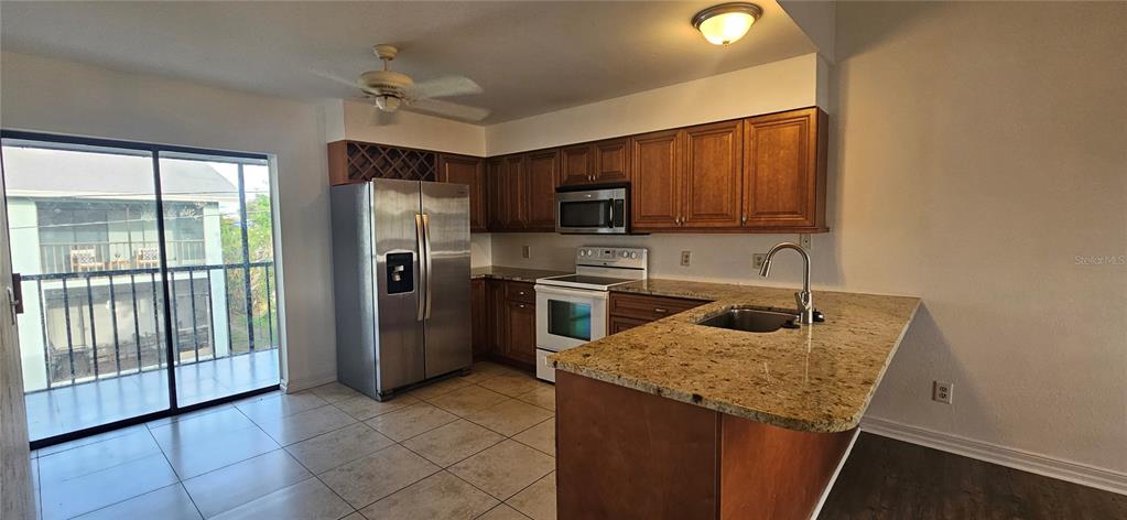 A kitchen features wood cabinets, granite countertops, stainless steel appliances, and a sliding glass door — 4904 VINCENNES COURT UNIT 209, CAPE CORAL, FL