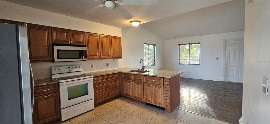 A kitchen with wood cabinets, granite countertops, and white appliances opens to a living area — 4904 VINCENNES COURT UNIT 209, CAPE CORAL, FL