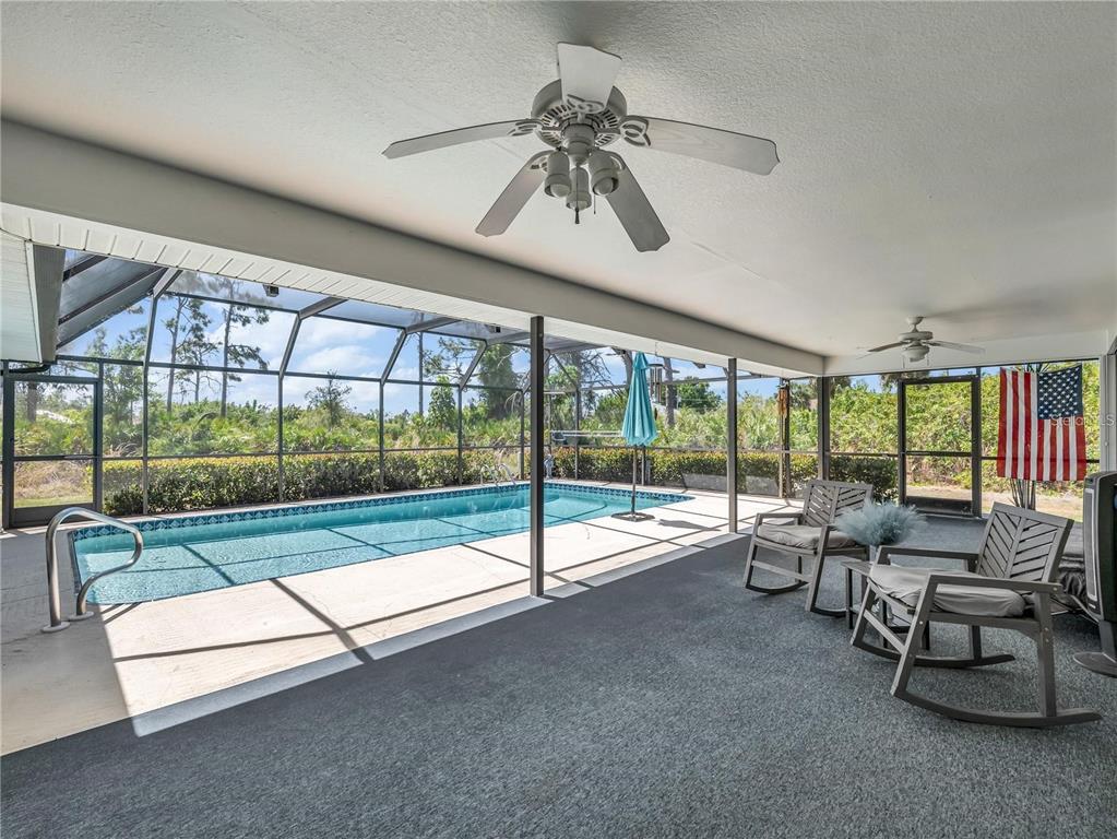 A covered patio features a swimming pool, two rocking chairs, and a ceiling fan — 6170 DAVID BOULEVARD, PORT CHARLOTTE, FL