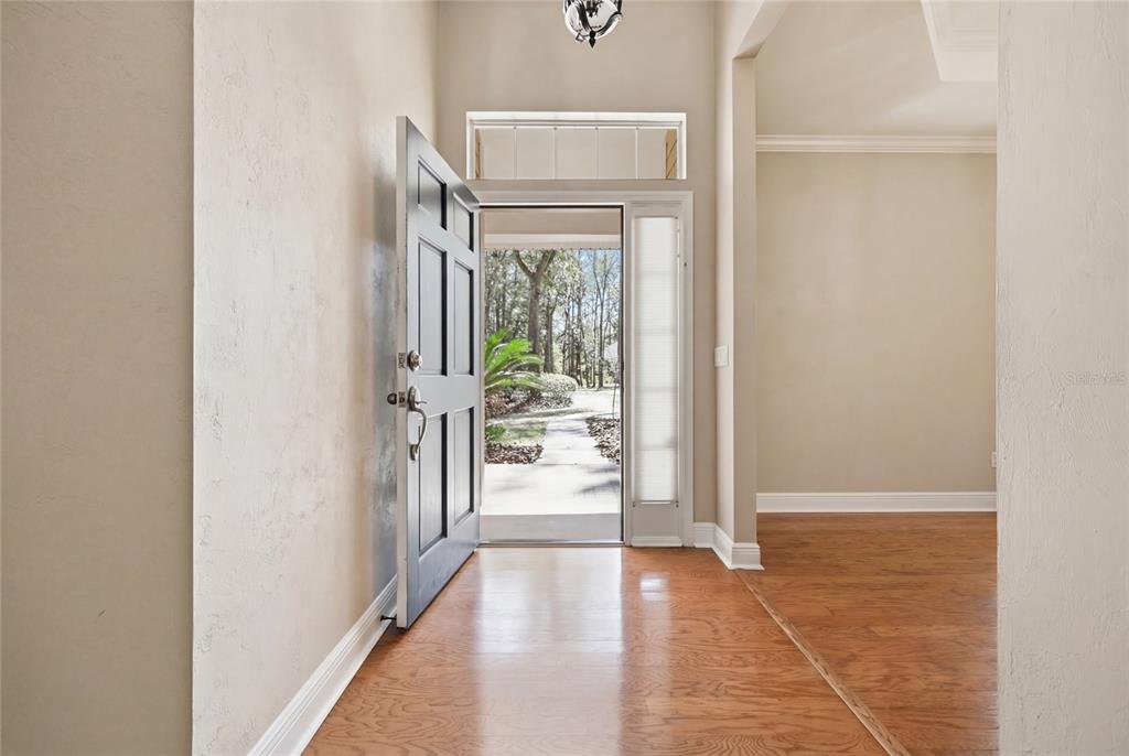 An open front door reveals a view of a wooded yard from a hardwood-floored entryway — 10320 SW 17TH PLACE, GAINESVILLE, FL