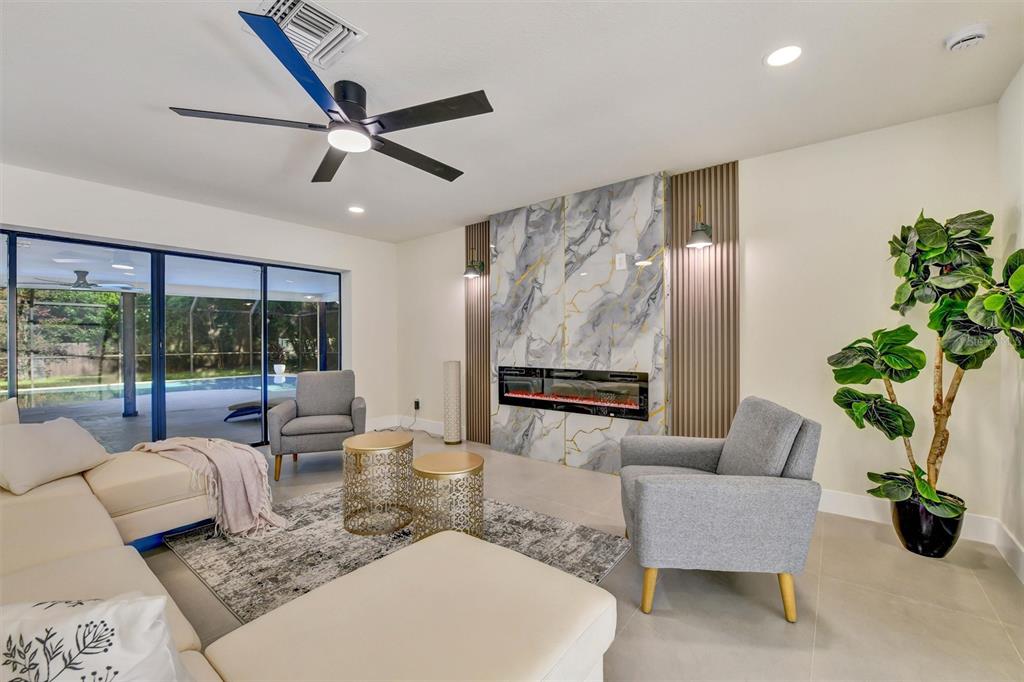 A living room features a marble fireplace, gray armchairs, a sectional sofa, and a ceiling fan — 207 DUNBRIDGE DRIVE, PALM HARBOR, FL