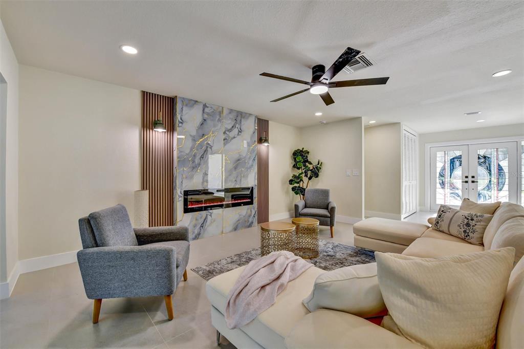 A living room features a marble fireplace, vertical wood slats, gray armchairs, and a sectional sofa — 207 DUNBRIDGE DRIVE, PALM HARBOR, FL