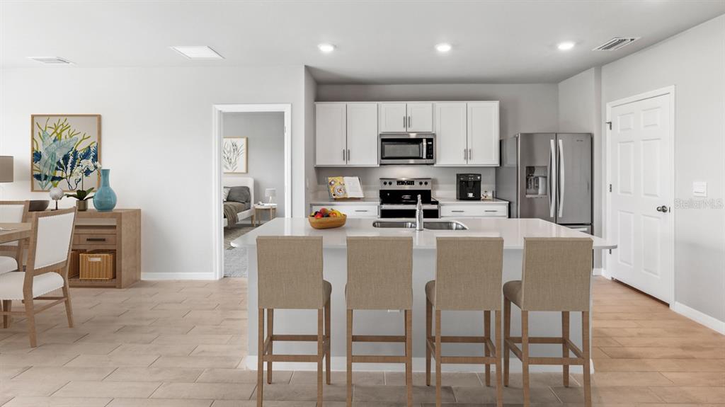 A modern kitchen features white cabinetry, stainless steel appliances, a center island, and bar seating — 26221 CORAL LAKES DRIVE, PUNTA GORDA, FL