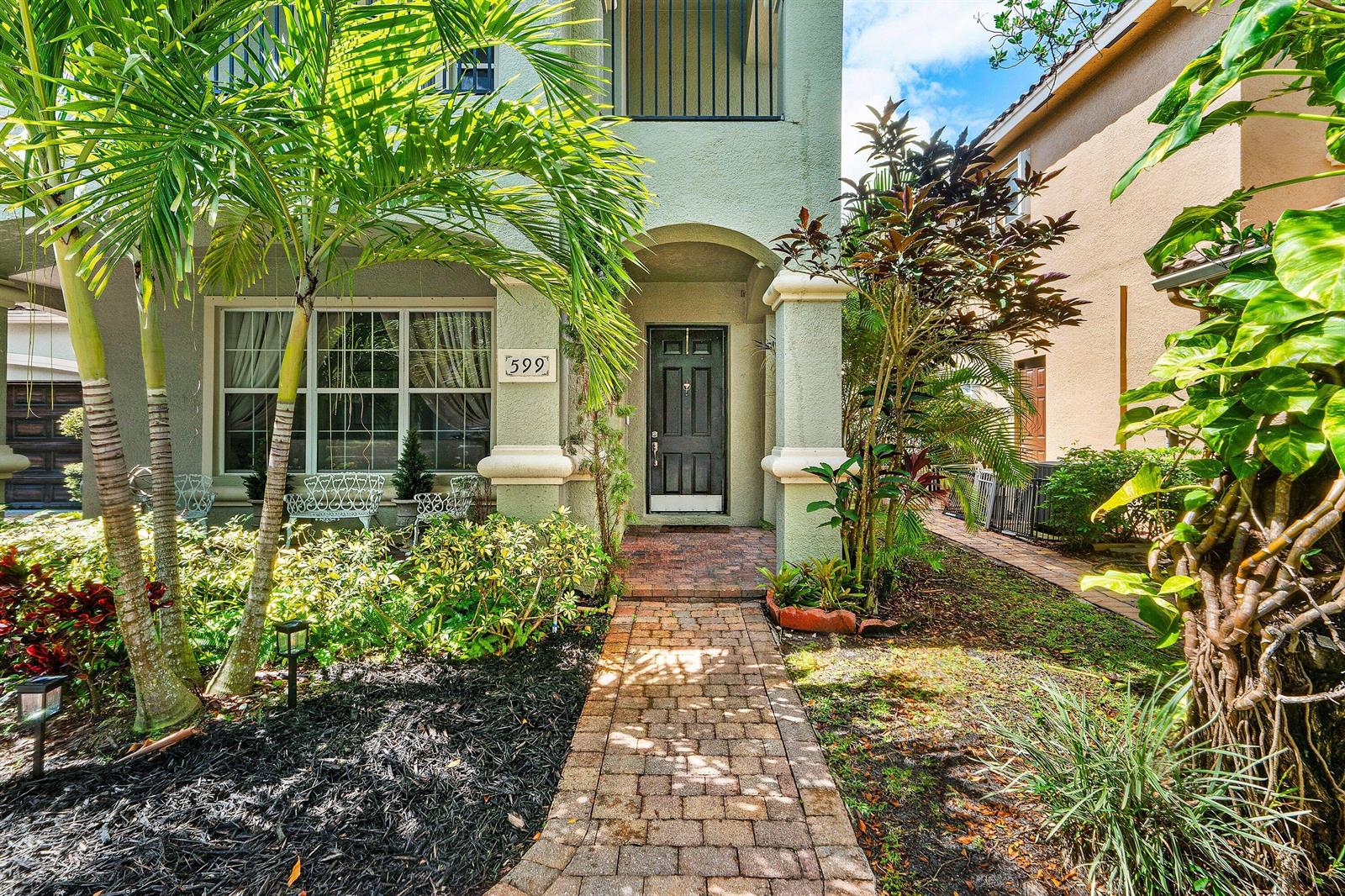 A brick walkway leads to the front entrance of a two-story house with palm trees — 599 Cresta Circle, West Palm Beach FL 33413, WEST PALM BEACH, FL