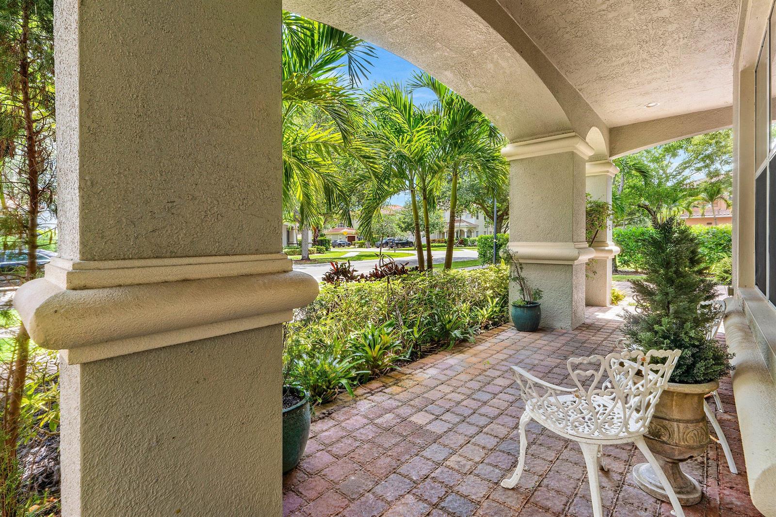 A covered brick patio features arched columns, potted plants, and a white metal chair — 599 Cresta Circle, West Palm Beach FL 33413, WEST PALM BEACH, FL