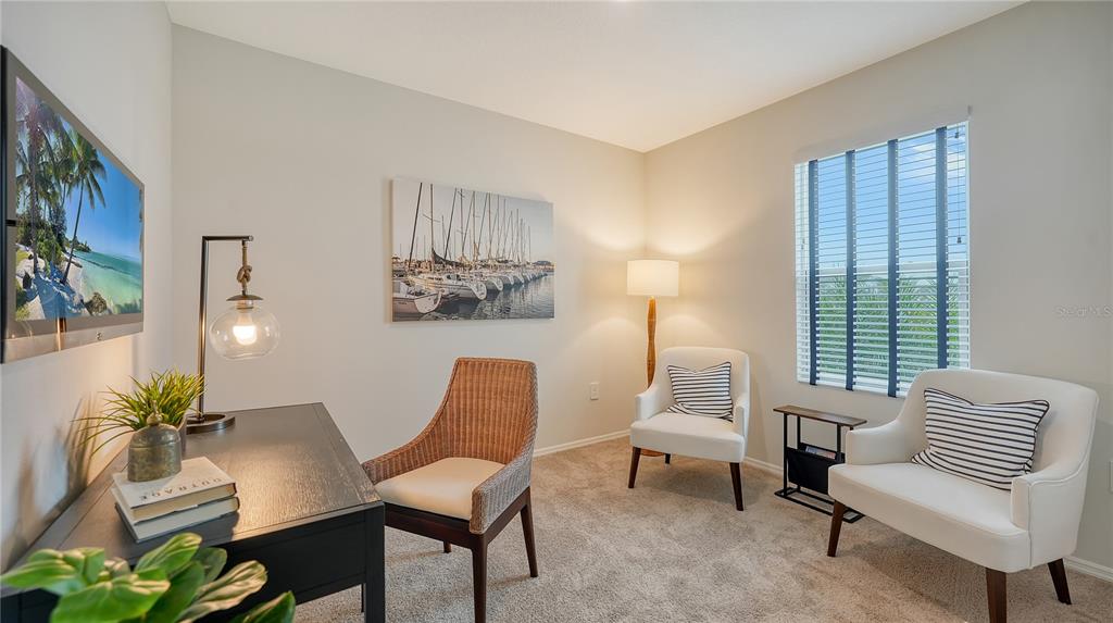 A home office features a dark desk, two white armchairs, and a sailboat wall art piece — 12919 RED DEER PLACE, PARRISH, FL