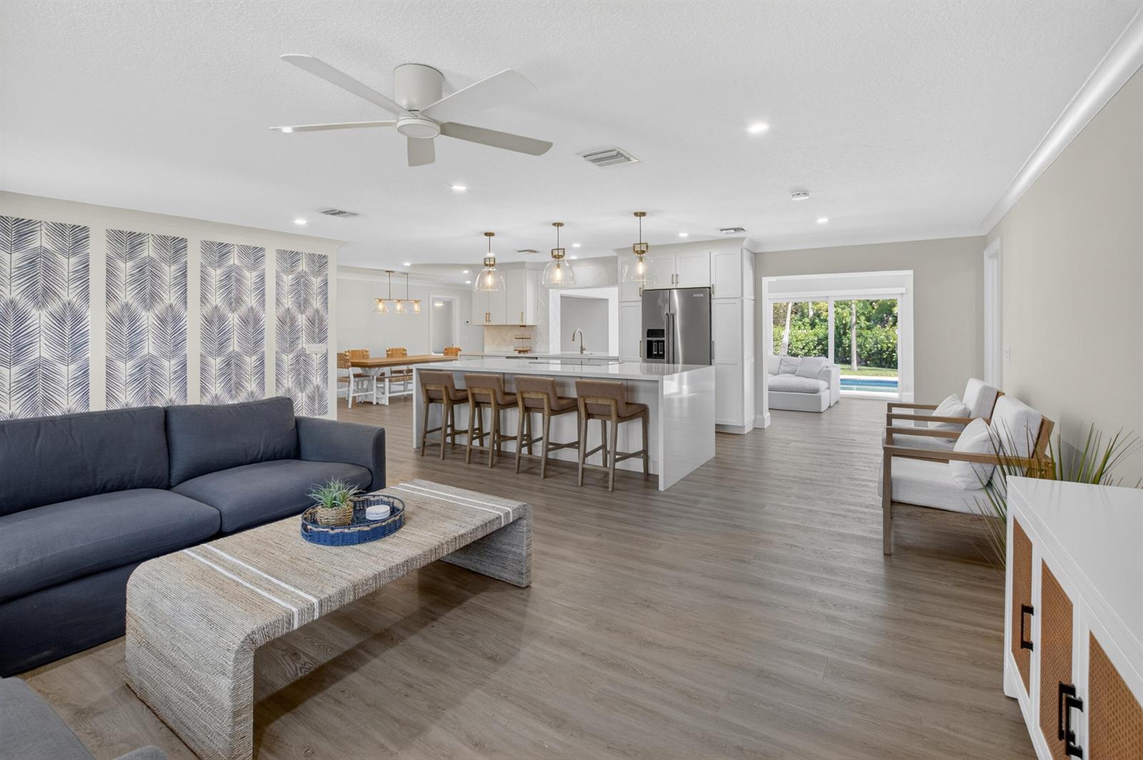 An open-concept living room and kitchen featuring a large island, gray sofa, and wood flooring — 135 SE 28th Court, Boynton Beach FL 33435, BOYNTON BEACH, FL