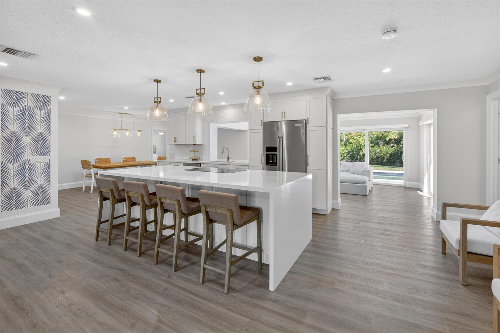 A modern kitchen features a large white island with bar seating and light wood flooring — 135 SE 28th Court, Boynton Beach FL 33435, BOYNTON BEACH, FL