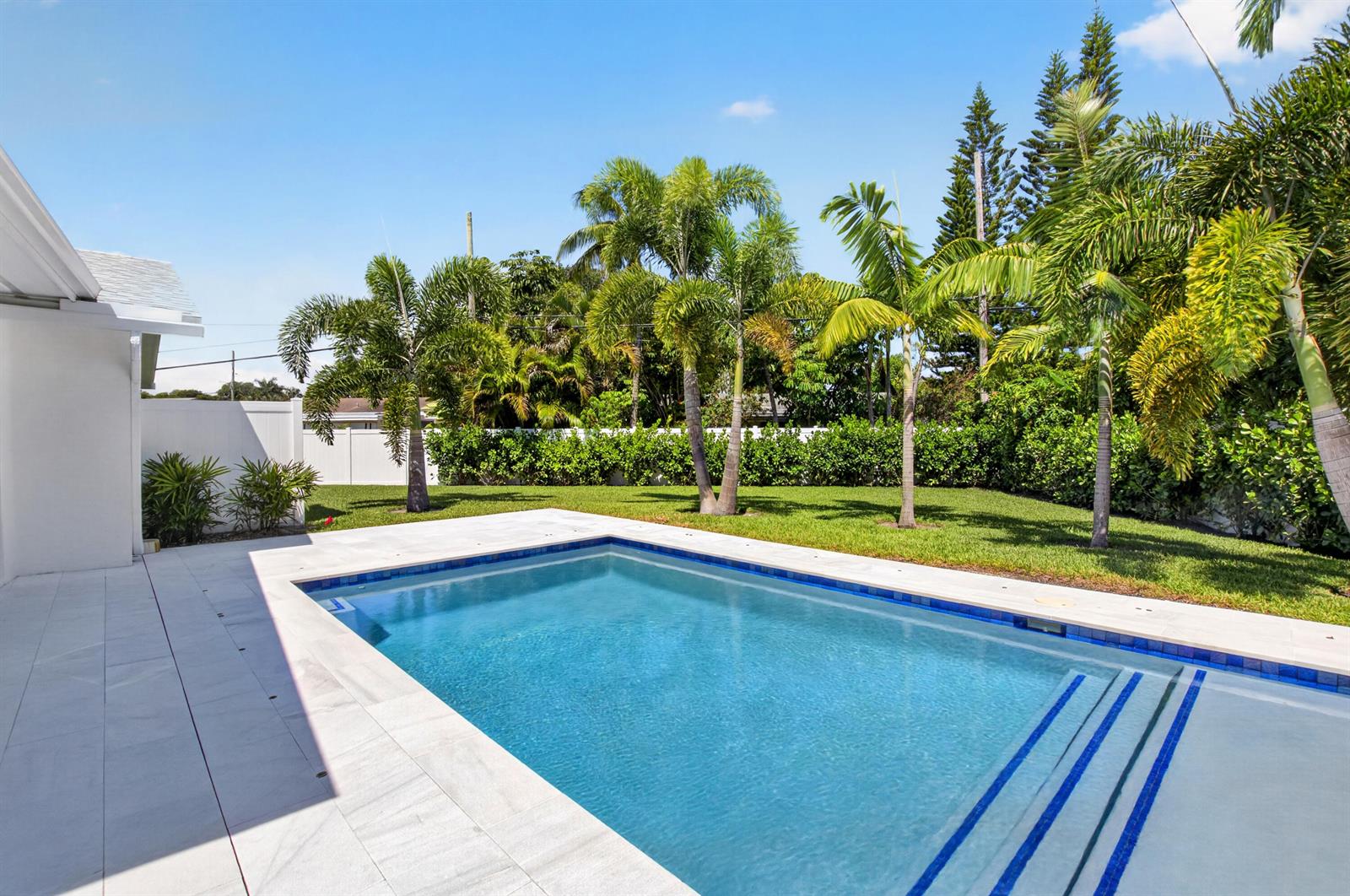 A backyard swimming pool with a white patio and palm trees on a sunny day — 135 SE 28th Court, Boynton Beach FL 33435, BOYNTON BEACH, FL