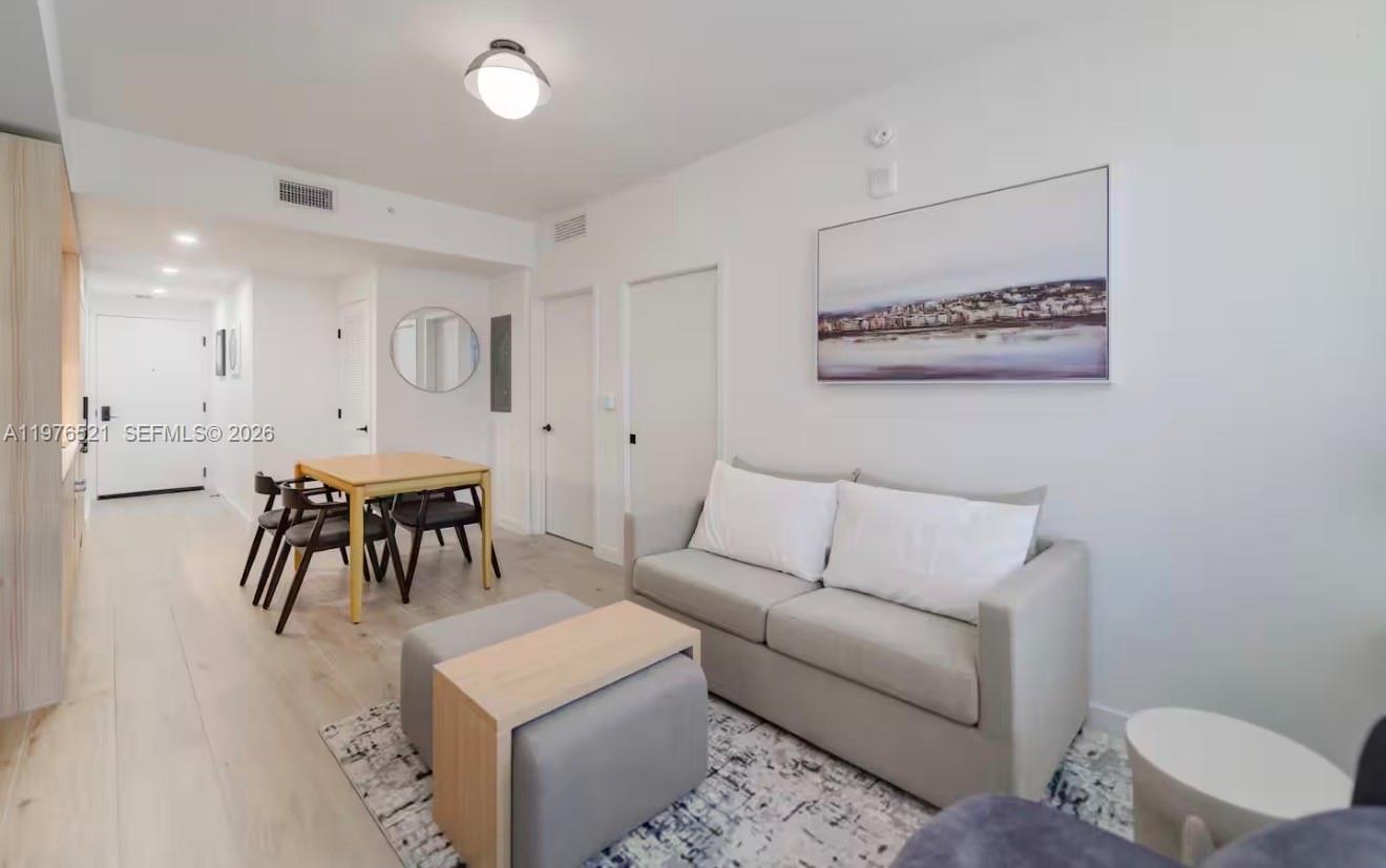 A living room features a grey sofa, a dining table, and light wood flooring — 225 N Miami Ave # 1103, Miami FL 33128, MIAMI, FL