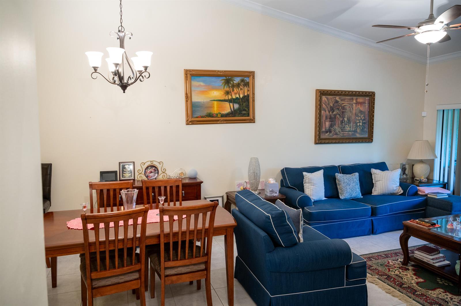 A dining area with a wooden table and chairs sits beside a living room with blue sofas — 7551 CAESAR Street # C, Lake Worth FL 33467, LAKE WORTH, FL