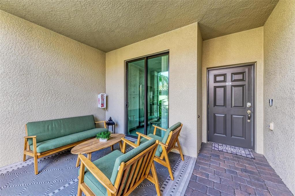 A covered patio features a sofa, two chairs, a coffee table, and a dark entry door — 5685 PALMER CIRCLE UNIT 105, BRADENTON, FL