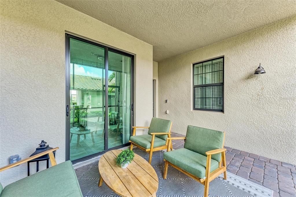 A covered patio features a paved floor, green chairs, a wooden coffee table, and sliding doors — 5685 PALMER CIRCLE UNIT 105, BRADENTON, FL