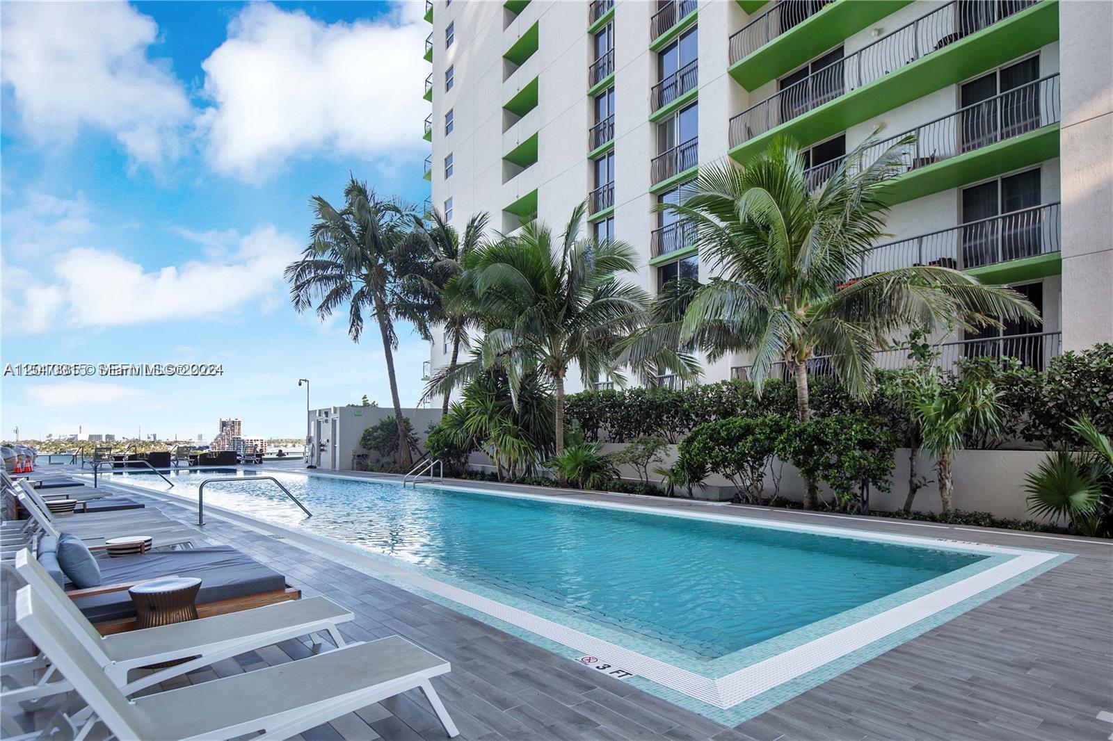 An outdoor swimming pool is surrounded by lounge chairs and palm trees beside a building — 488 NE 18th St # 301, Miami FL 33132, MIAMI, FL