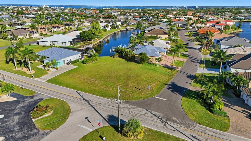 An aerial view shows a vacant grassy lot situated between two residential streets and a canal — 600 VIA TRIPOLI, PUNTA GORDA, FL