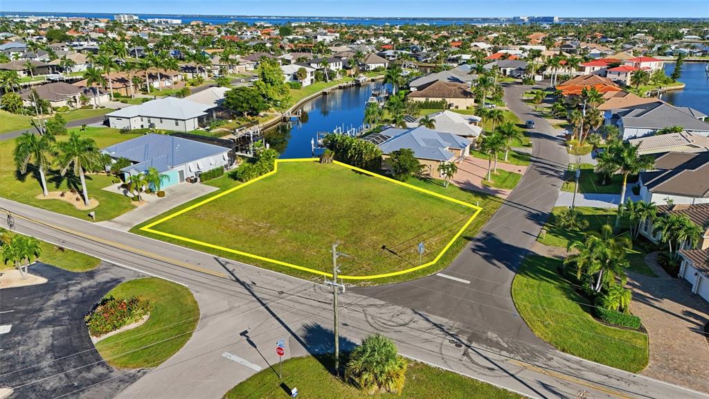 An aerial view shows a vacant, yellow-outlined corner lot situated between two residential streets — 600 VIA TRIPOLI, PUNTA GORDA, FL