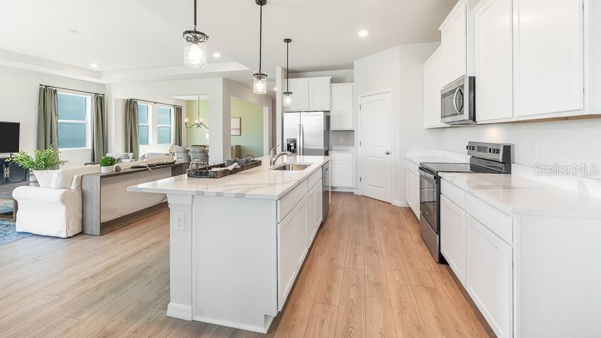 A modern kitchen features white cabinetry, a large marble-topped island, and light wood flooring — 10433 WOODLAND GARDEN WAY, PARRISH, FL
