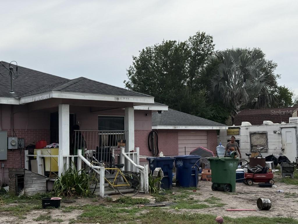 An exterior view of a pink house with a front porch, yard, and various items — 5207 E 20TH AVENUE, TAMPA, FL