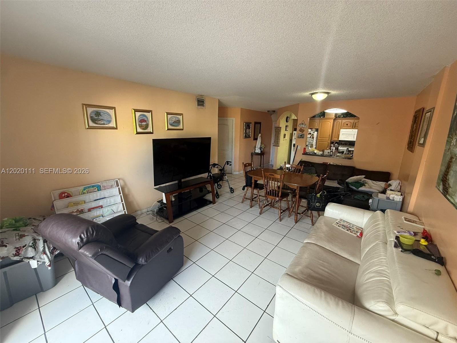 A living and dining area features peach walls, white tile floors, and a kitchen pass-through — 6780 W 2nd Ct # 313, Hialeah FL 33012, HIALEAH, FL