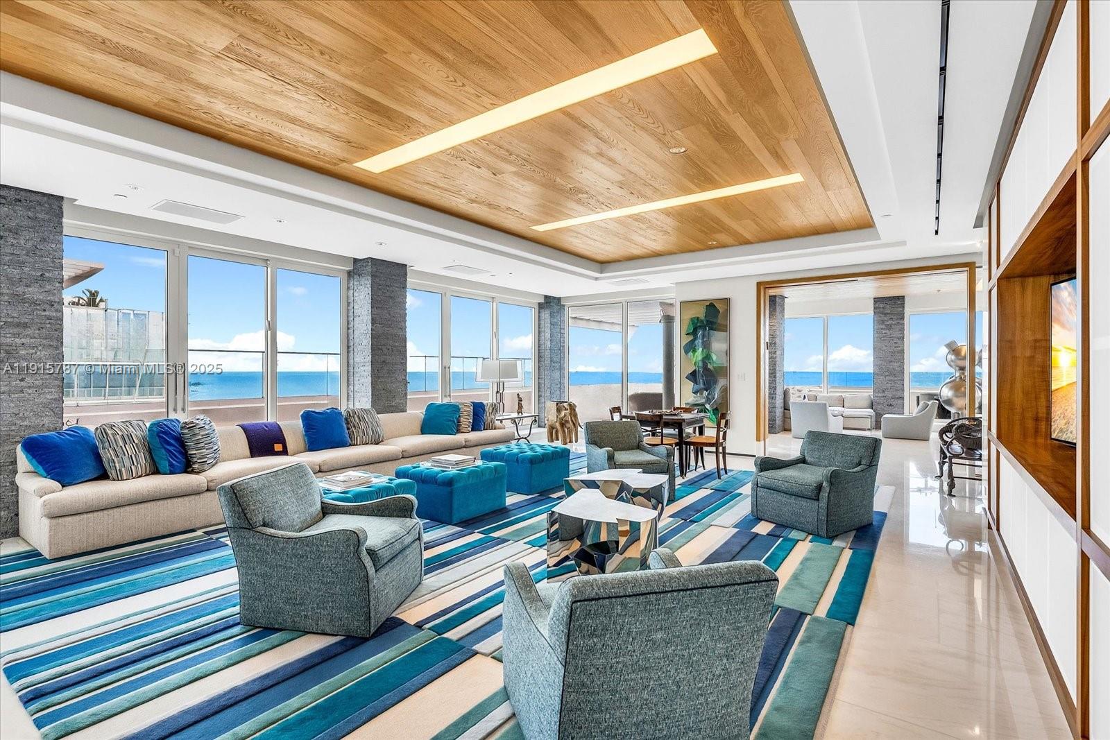 A spacious living room features a wood-paneled ceiling, blue-toned furniture, and floor-to-ceiling ocean views — 430 Grand Bay Dr, Key Biscayne FL 33149, KEY BISCAYNE, FL