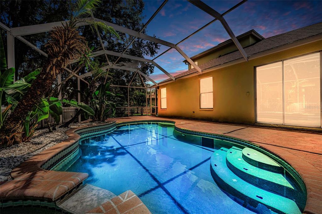 A screened-in swimming pool with tiered steps sits beside a house at twilight — 3052 SUNWATCH DRIVE, WESLEY CHAPEL, FL