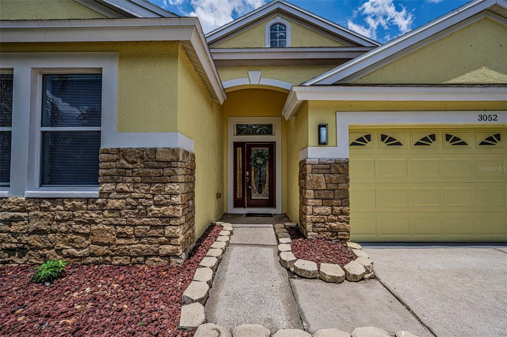 The exterior of a yellow house features stone veneer, a garage, and a front entrance — 3052 SUNWATCH DRIVE, WESLEY CHAPEL, FL