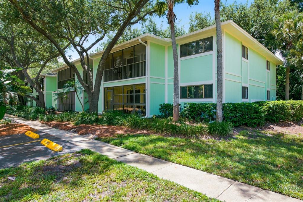 A two-story apartment building with light green siding, screened balconies, and a paved parking area — 3295 FOX CHASE CIRCLE N UNIT 207, PALM HARBOR, FL