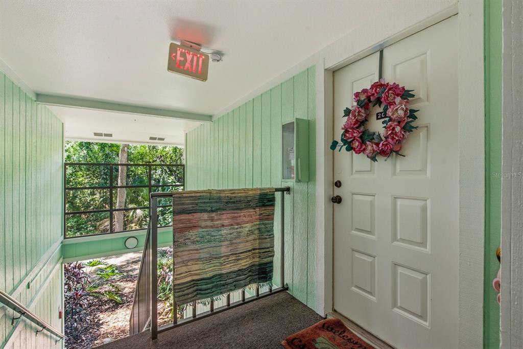 A light green hallway leads to a white door adorned with a floral wreath — 3295 FOX CHASE CIRCLE N UNIT 207, PALM HARBOR, FL