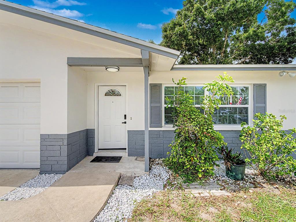 A white house exterior features a gray stone base, a front door, and a window — 1354 ROSERY ROAD NE, LARGO, FL