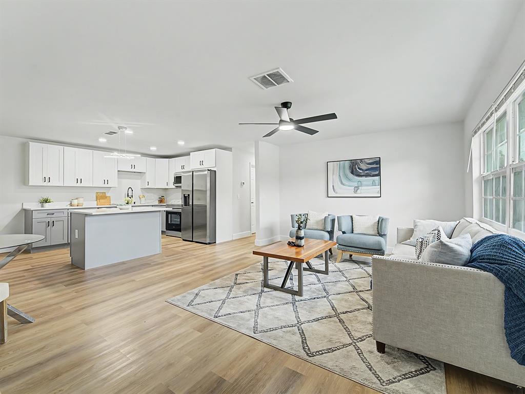 An open-concept living room and kitchen feature light wood flooring, white cabinetry, and neutral furniture — 1354 ROSERY ROAD NE, LARGO, FL