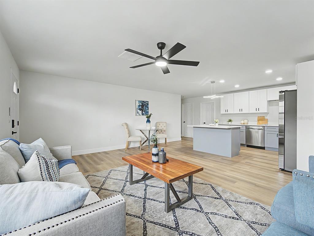 An open-concept living room and kitchen feature light wood flooring and white cabinetry — 1354 ROSERY ROAD NE, LARGO, FL