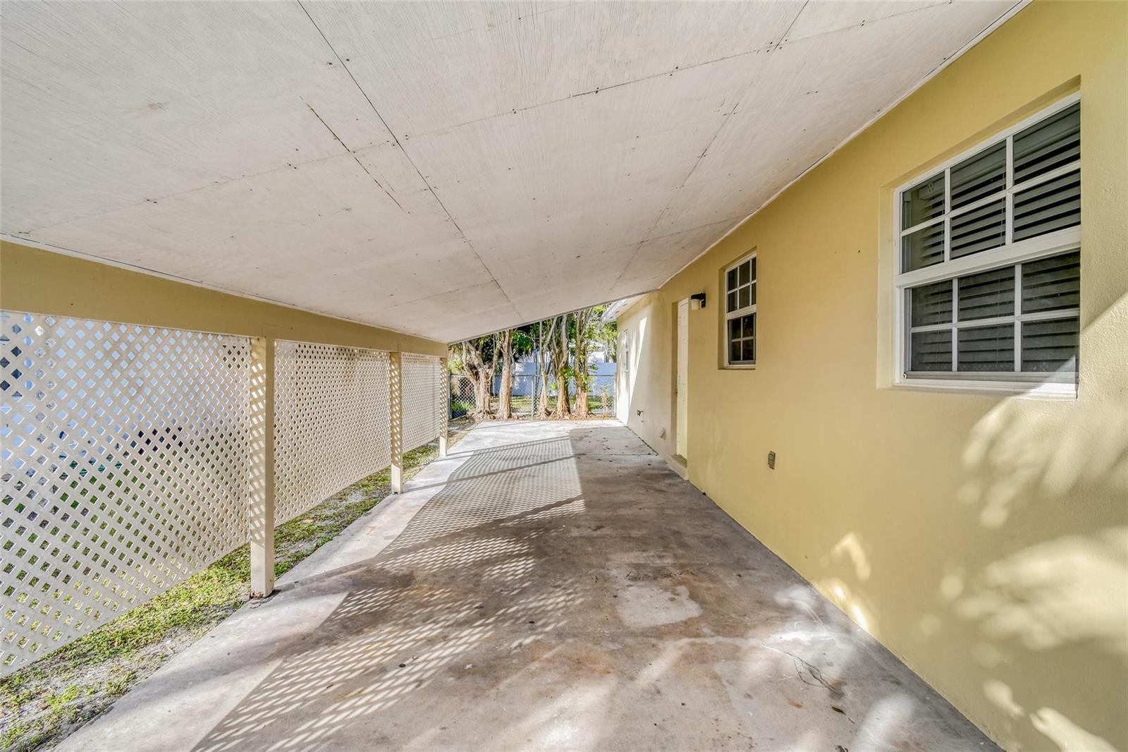 A covered concrete patio features a white lattice privacy screen and yellow exterior walls — 1227 Cherokee Street, Jupiter FL 33458, JUPITER, FL